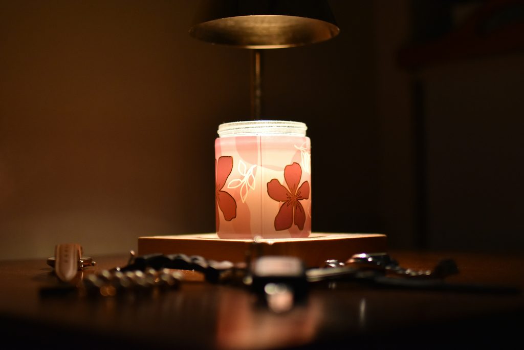 Candle warmer lamp melting a floral jar candle on a wooden table in a warm, dimly lit room.